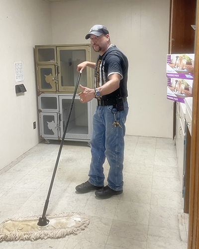 A man cleans the floor of an animal shelter with a mop.