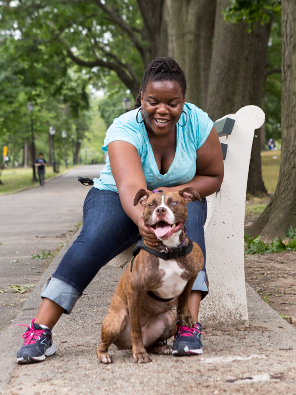 a woman sitting on a bench in a park petting a dog