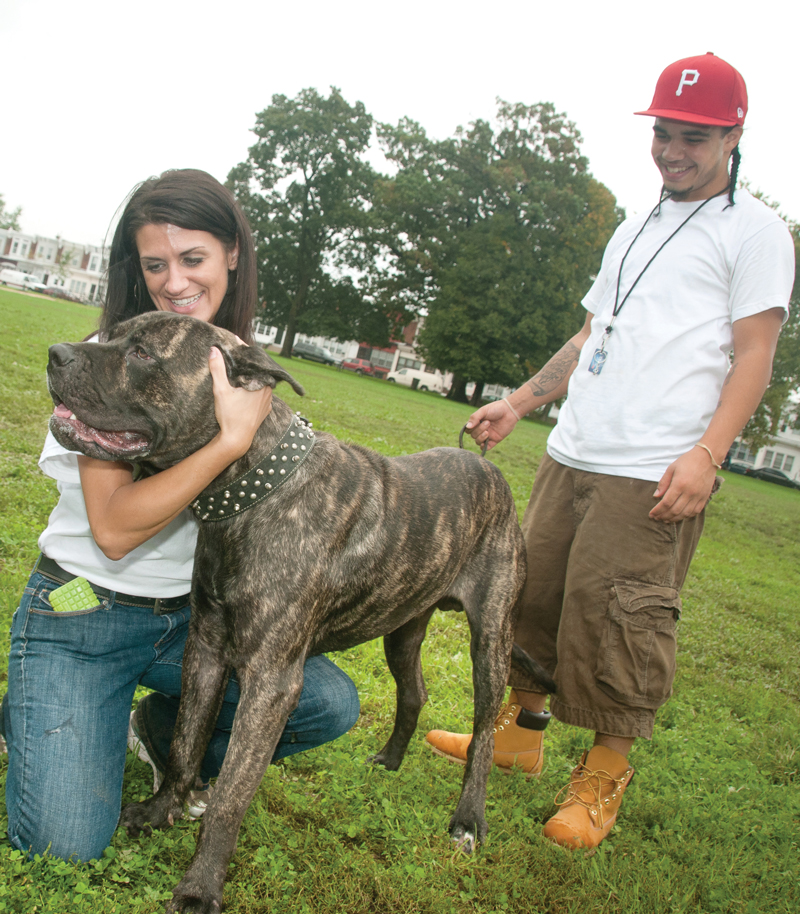 a woman kneels to hug a large dog while its owner looks on