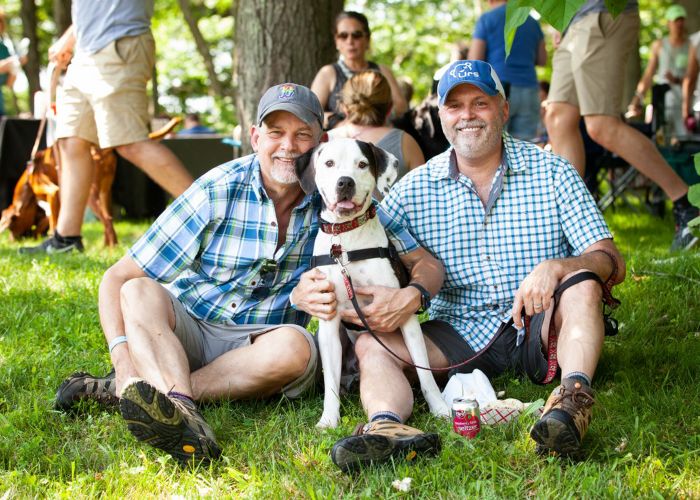 Two men pose with their dog at an outdoor event