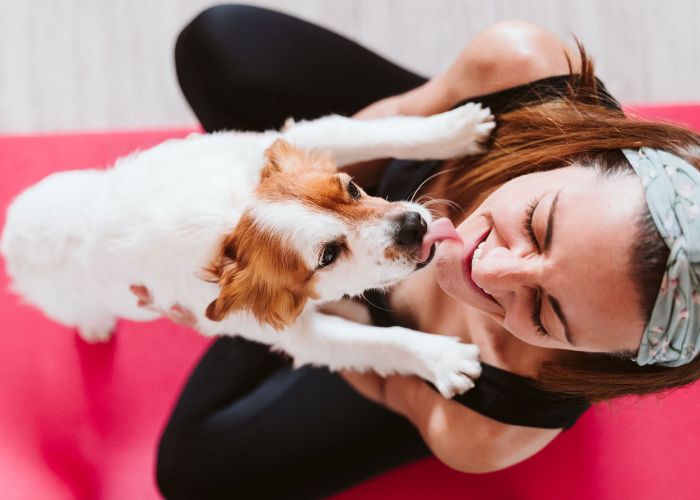 Photo of a dog licking a woman's face while she's on a yoga mat.