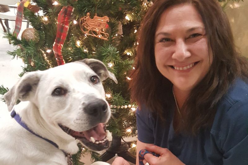 a smiling woman poses next to a white dog in front of a Christmas tree