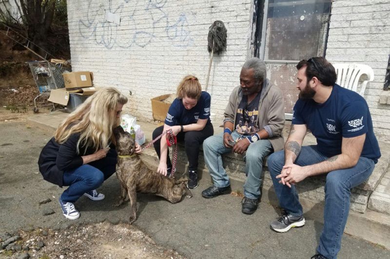 four people gathered around a dog in an impoverished area