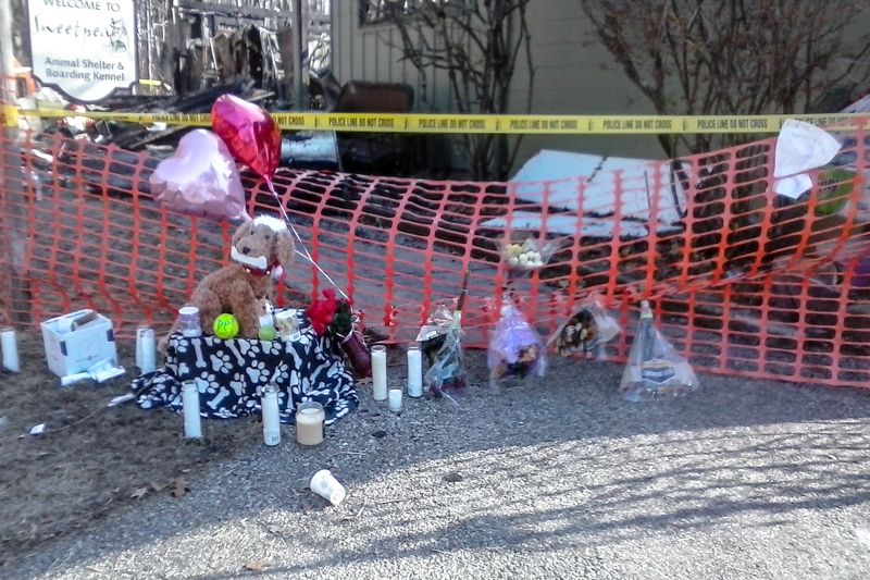 candles, stuffed animals, and other mementos are gathered around a line of police tape