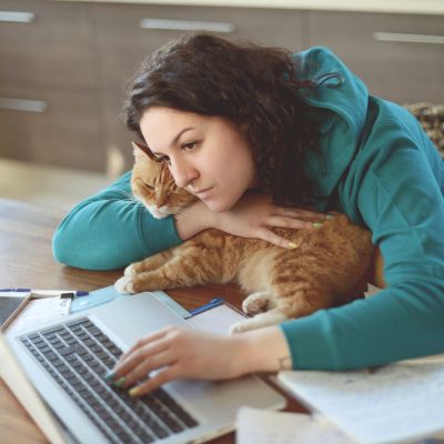Sad woman hugging a cat while on her laptop computer.
