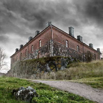 a dilapidated building on an overgrown hill with storm clouds overhead