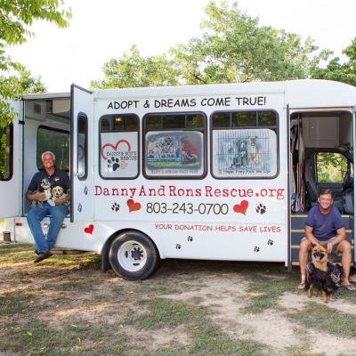 two men and their dogs sit alongside their rescue bus