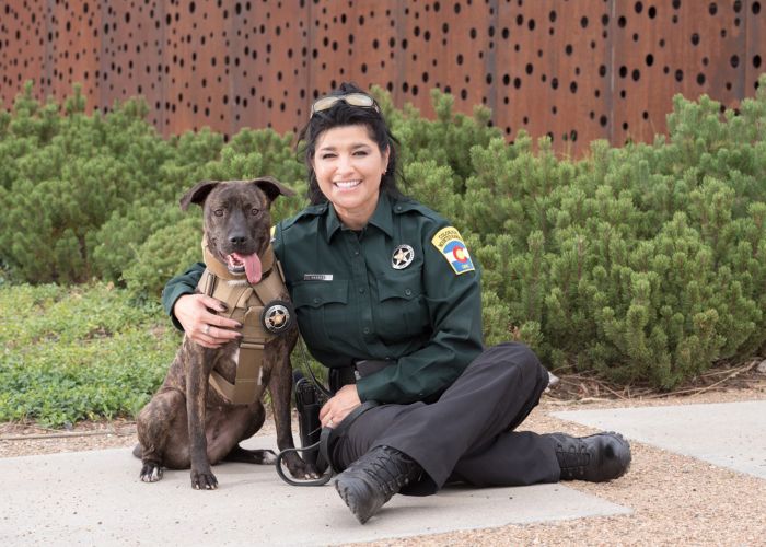 a woman in uniform poses next to a dog in a bullet-proof vest