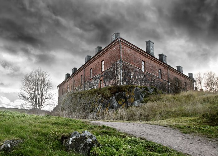 a dilapidated building on an overgrown hill with storm clouds overhead