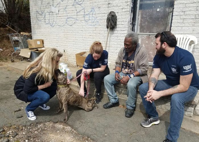 four people gathered around a dog in an impoverished area