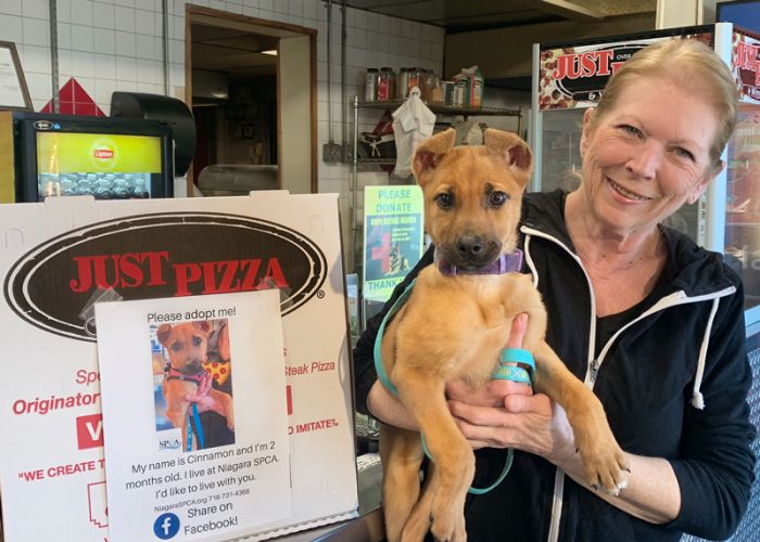 a woman holds a puppy in front of a pizzeria